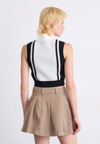Svart och vit ärmlös stickad topp med hög krage, med två vertikala vita ränder på baksidan och en figurnära silhuett, tillsammans med beige veckade shorts.