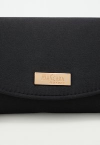 Czarna torebka kopertówka z zaokrąglonym klapkiem i prostokątną złotą plakietką z wygrawerowanym logo "Mascara London" z przodu.