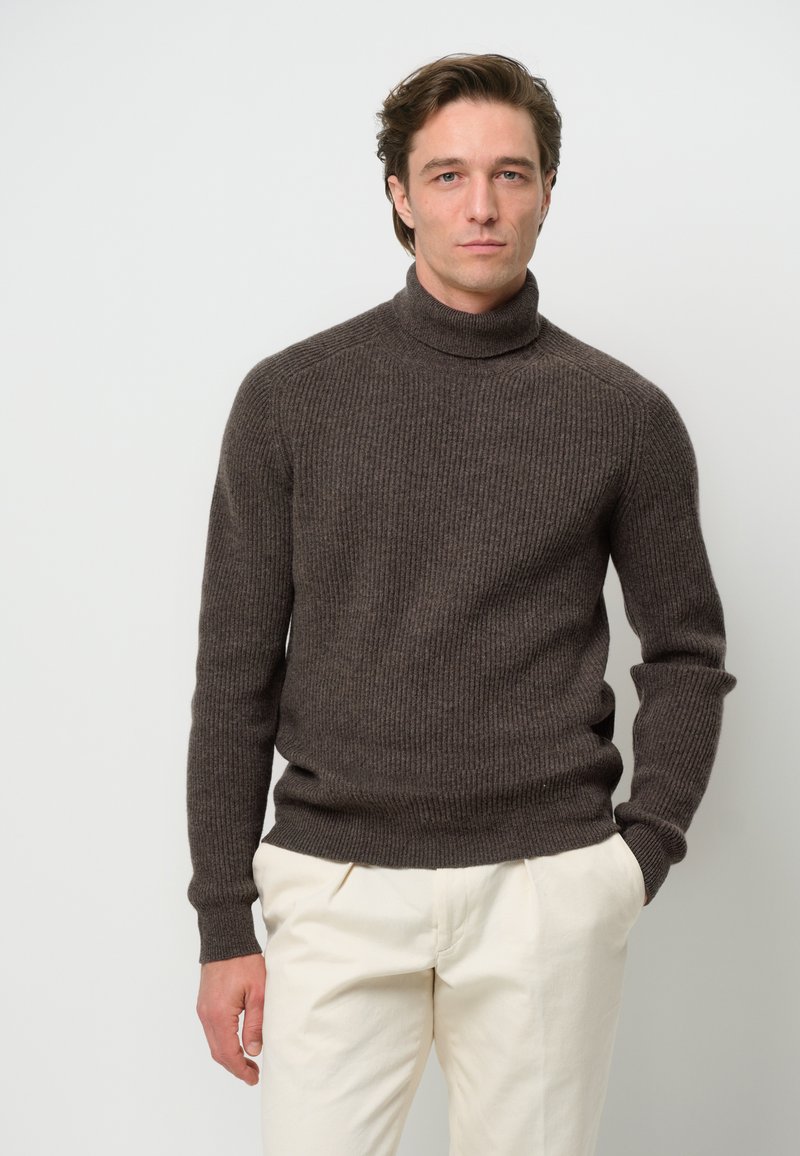 Brauner gerippter Rollkragenpullover aus einem weichen Wollgemisch, taillierter Schnitt, mit umgeschlagenem Kragen und langen Ärmeln, kombiniert mit hellen Hosen.