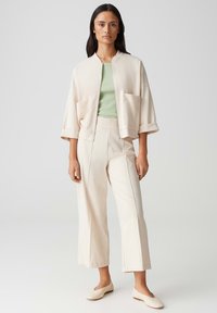 Lichte crème bomberjack met twee voorzakken, gecombineerd met een aansluitend groene top en bijpassende crème wijde broek. Soepele textuur.