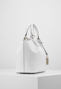 Sac à main en cuir blanc avec une forme douce et arrondie, présentant des finitions en métal doré, un accent de serrure en argent et des bords noirs contrastants.