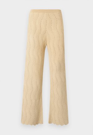 Pantalon en maille beige à jambes larges, présentant un motif chevrons avec de petits trous et un ourlet festonné.