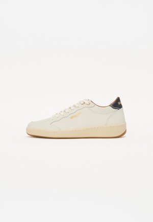 Baskets en cuir beige avec une surface texturée, bout rond, lacets blancs et semelle en caoutchouc beige. Présente un accent de talon bleu marine et un logo doré.
