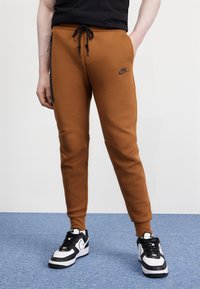 Smešane smeđe trenirke s crnim trakama sa strane, elastična pojas s žicom za stezanje i Nike logo. Nositi s crno-bijelim tenisicama.