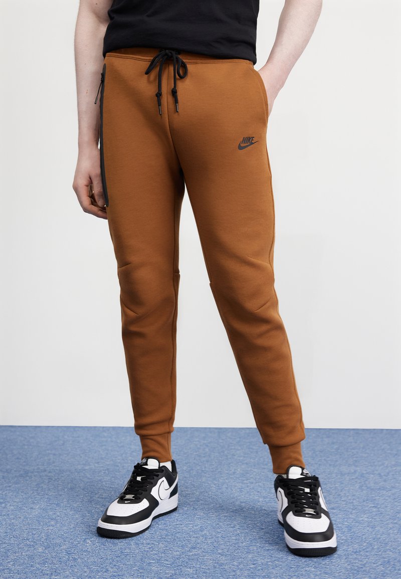 Smešane smeđe trenirke s crnim trakama sa strane, elastična pojas s žicom za stezanje i Nike logo. Nositi s crno-bijelim tenisicama.