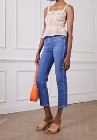 Kostkovaná peplum blůza v oranžové, žluté a modré barvě, spárovaná se světle modrými džíny. Béžové semišové muly na bloku a malá oranžová kabelka.