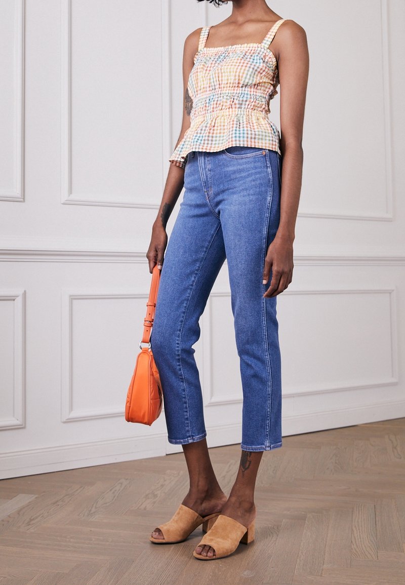 Kostkovaná peplum blůza v oranžové, žluté a modré barvě, spárovaná se světle modrými džíny. Béžové semišové muly na bloku a malá oranžová kabelka.