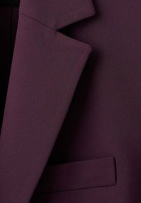 Tissu de blazer bordeaux avec une texture lisse, arborant un revers cranté, une poche unique et des détails de couture soignés.