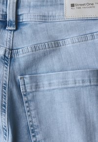 Un jean en denim bleu clair présente un design classique avec des coutures visibles et une poche arrière. Une étiquette avec "Street One" est attachée.