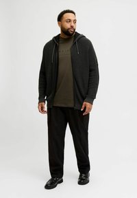 Czarna dzianinowa bluza z kapturem na zamek z teksturowanym wzorem, zestawiona z ciemnooliwkowym t-shirtem i czarnymi spodniami o luźnym kroju, uzupełniona czarnymi butami.