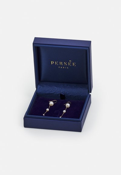 Kultaketjuhansikkaat valkoisilla helmillä, esitelty navy-sinisessä laatikossa, jossa on kultakirjoitus ja pehmeä navy-sininen sisustus.