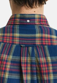 Overhemd met een blauw ruitpatroon en rode en gele accenten, gelegen aan de achterkant met een plissé-detail en versterkte halslijn.