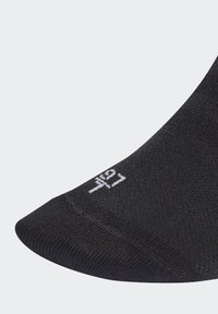 Calcetín negro hasta el tobillo con una superficie texturizada, que presenta un logo blanco en la puntera. El diseño tiene una forma ajustada para mayor comodidad.