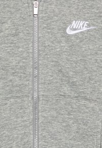 Grå zip-up hoodie i mjukt tyg med texturerad yta. Har en framträdande Nike-logotyp i vitt och en silverfärgad metalldragkedja.