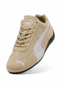 Μπεζ αθλητικό παπούτσι από σουέντ με κορδόνια, λευκά διακοσμητικά στη πλευρά και μαύρη ελαστική σόλα. Το λογότυπο της Puma εμφανίζεται στη γλώσσα και στη πλευρά.