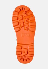 Semelle de chaussure en caoutchouc orange vif, arborant une surface texturée et motifée avec de profondes rainures et le logo 'CAMPER' en relief près du talon.
