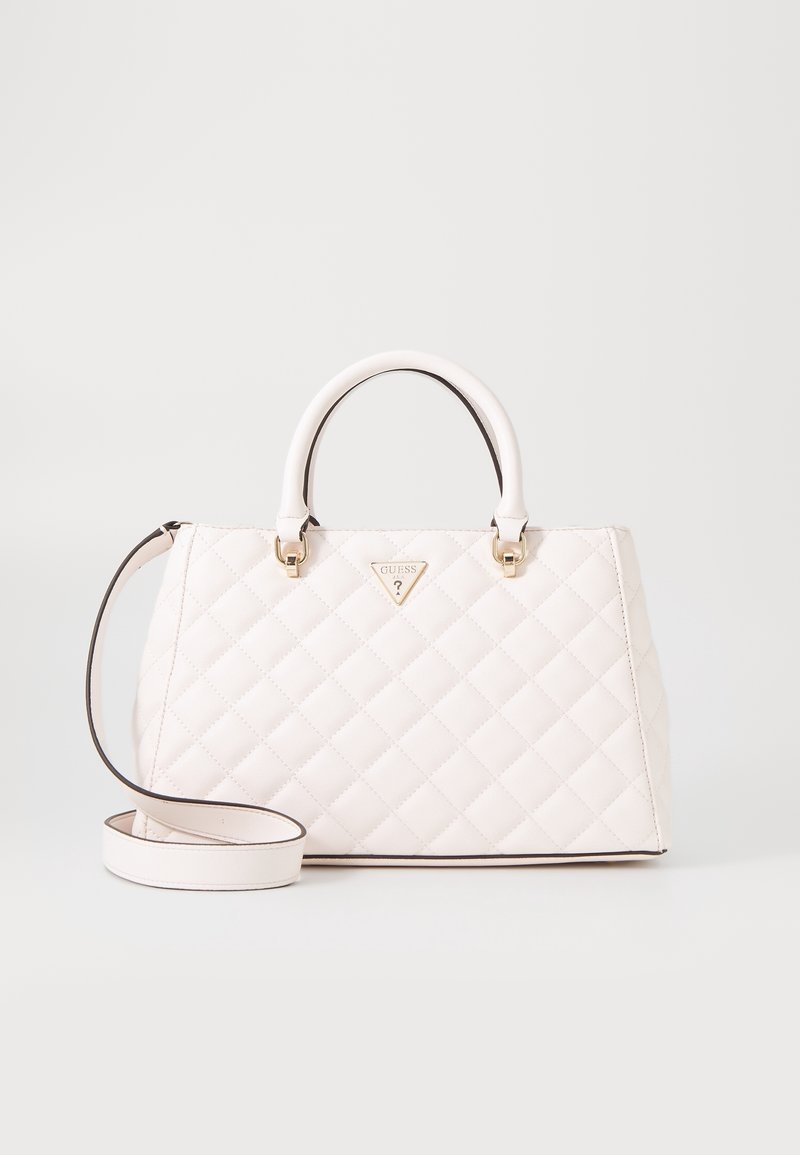 Sac à main matelassé blanc avec poignées supérieures et longue bandoulière, orné d'une petite plaque triangulaire avec le logo Guess au centre devant.