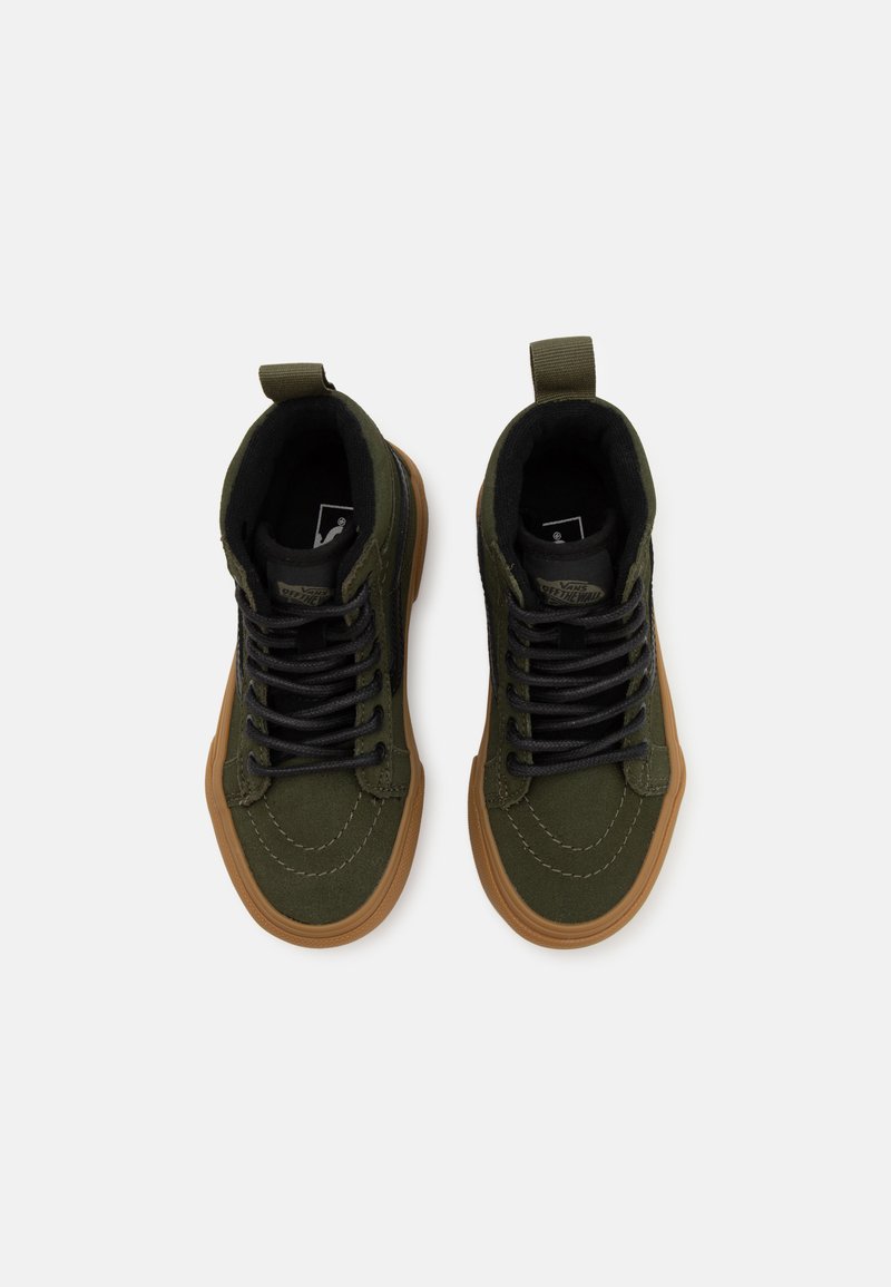 Zapatillas altas de lona verdes con cordones negros, suela de goma marrón y una correa trasera. Presentan un material texturizado y detalles de costura.