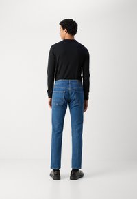 Mørk langærmet skjorte parret med mellem-høj talje blå denim jeans, der har lige snit, to baglommer og diskrete syninger.