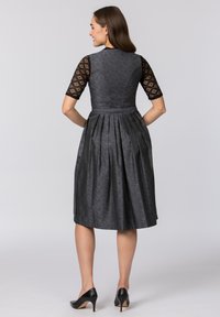 Black dress with textured fabric, short lace sleeves, and a pleated skirt. Features a fitted bodice and a smooth waistband. Black heels.