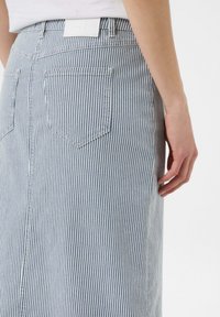 Niebieska i biała spódnica jeansowa w paski, z dwiema tylnymi kieszeniami, o długości średniej i widocznym przeszyciu. W talii zaakcentowana białą metką.