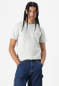 Grå kortærmet t-shirt i et blødt stof med et lille logo på venstre bryst. Båret med blå denimbukser.