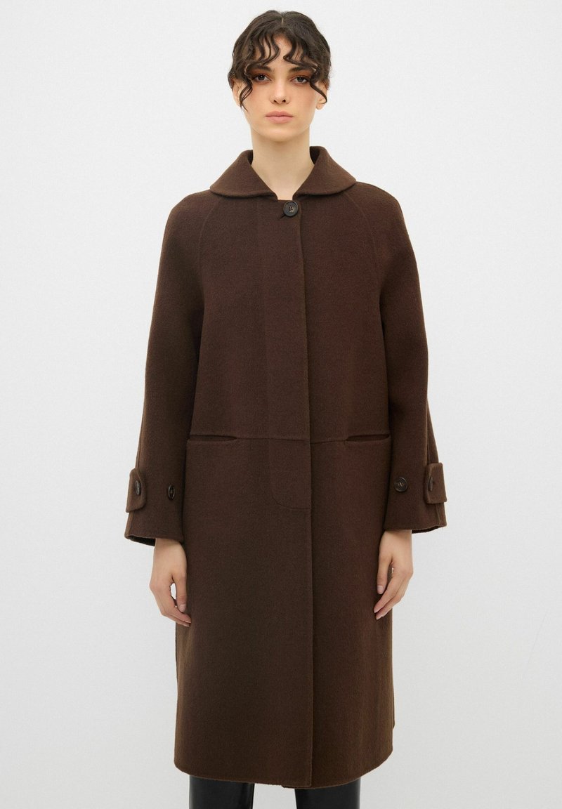 Cappotto in lana marrone con colletto arrotondato, chiusura a bottoni e due tasche frontali. Presenta maniche lunghe e polsini con bottoni.