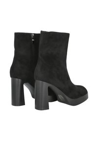 Botines de ante negro hasta el tobillo con tacones altos gruesos y cierres de cremallera laterales, exhibidos sobre un fondo blanco.