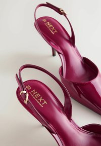 Escarpins à talons aiguilles slingback en cuir verni fuchsia avec un bout pointu et un talon stiletto fin. Comprend une boucle couleur or sur la bride réglable.