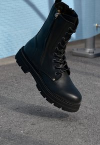 Zwarte leren enkelboot met een veterfront, zijrits en robuuste zool. Heeft een gladde afwerking en stevige hardwaredetails.