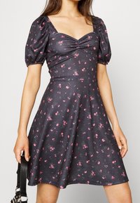 Černé květinové šaty s krátkými nafouknutými rukávy, čtvercovým výstřihem, nařaseným živůtkem, vypasovaným pasem a rozšířenou sukní s růžovými a zelenými květinovými vzory.