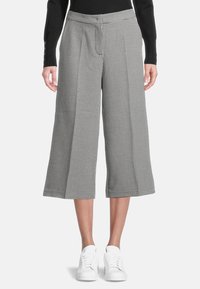 Černobílé kalhoty s kostkovaným vzorem a širokými nohavicemi do délky kotníků, obuté s bílými teniskami a černým topem s dlouhým rukávem.