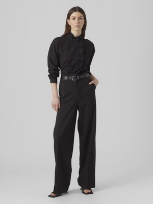 Camicia nera con bottoni e volant sul davanti, abbinata a pantaloni neri a vita alta e gamba larga, con una cintura nera elegante.