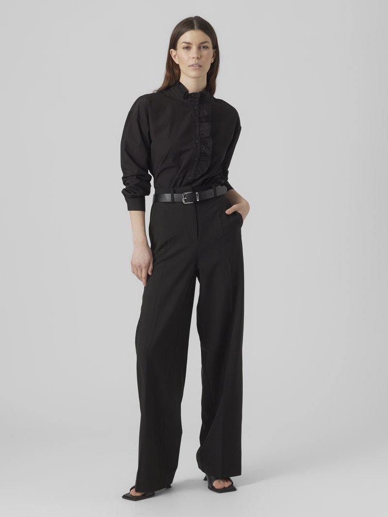 Camicia nera con bottoni e volant sul davanti, abbinata a pantaloni neri a vita alta e gamba larga, con una cintura nera elegante.