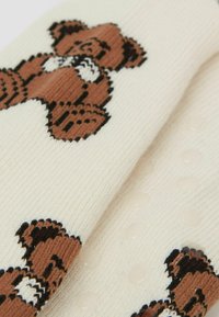 Cremefarbene Socken mit braunen Teddybär-Motiven, gestrickter Textur mit erhabenen Punkten für Halt und schwarzen Konturen auf den Bären.