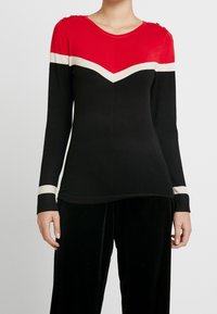 Langärmeliges Oberteil in Rot, Schwarz und Creme. Mit einem Zickzackmuster, Schulterknöpfen und kontrastierenden Bündchen in Creme.