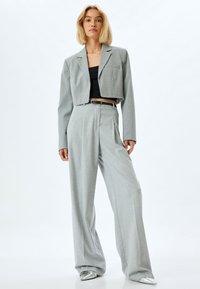 Grijze cropped blazer en wijde broek van textuurstof, gecombineerd met een zwarte top en zilveren schoenen. De outfit heeft een riem.