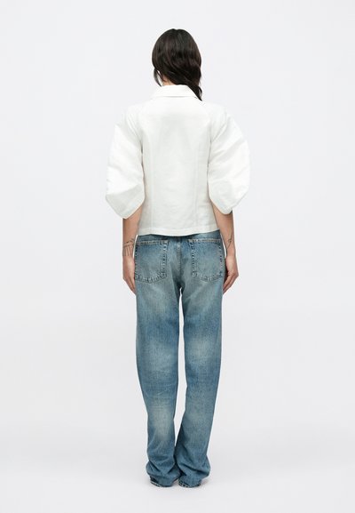 Λευκή μπλούζα με φουσκωτά μανίκια και γιακά, σε συνδυασμό με ανοιχτό μπλε τζιν παντελόνι ίσιας γραμμής με διακριτική ξεθώριαση, πίσω τσέπες και άνετη εφαρμογή.