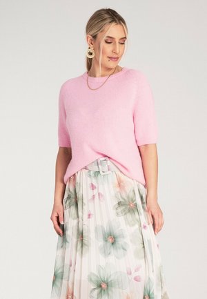 Jasnoróżowy sweter z krótkim rękawem o miękkiej fakturze, połączony z plisowaną spódnicą w kwiatowy wzór w delikatnych pastelowych kolorach oraz jasnoszarym paskiem.