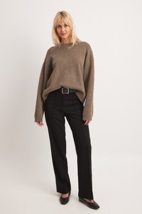 Hnedý, prehnaný pletený sveter s dlhými rukávmi; kombinovaný s čiernymi nohavicami rovného strihu a čiernymi balerínkami. Jednoduchý strieborný detail spona na opasku.