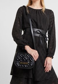 Černá prošívaná kabelka přes rameno se zlatým logem "LOVE MOSCHINO", vybavená hladkým koženým popruhem a strukturovaným, zaobleným tvarem.