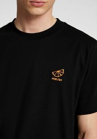 Svart bomull T-shirt med rund halsringning, med en orange broderad grafik av en citrusfruktsskiva och ordet "SELECTED" nedanför.