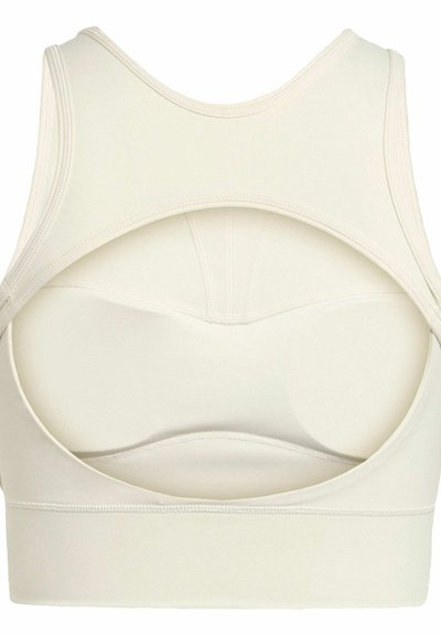 Sujeción deportiva color beige claro con un diseño de espalda redonda, tejido suave, tirantes anchos y detalles de costura vertical. Textura suave y sin costuras.