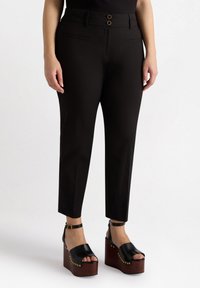 Zwarte op maat gemaakte broeken met een hoge taille, voorzien van twee decoratieve knopen en zijzakken. Gemaakt met zwarte plateau-sandalen.