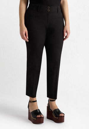 Pantaloni neri su misura con vita alta, caratterizzati da due bottoni decorativi e tasche laterali. Indossati con sandali platform neri.