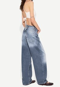 Ljusblå vida denimjeans med en blekt finish, fem fickor och en avslappnad passform, tillsammans med mörkbruna platta skor.