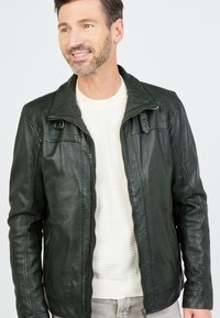 Donkergroene leren jas met een ritssluiting aan de voorkant, staande kraag en twee zijzakken. Kenmerkt zich door een gestructureerd oppervlak en subtiele stikdetails.