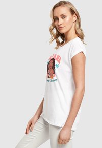 Hvid bomulds t-shirt med korte, optrækkede ærmer, der har et farverigt grafik af en kvinde med tropiske elementer og teksten "Altid på din rejse".
