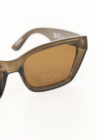 Lunettes de soleil teintées marron avec une monture translucide marron, comportant un label de protection UV 400. Forme angulaire avec un design de branches épurées.