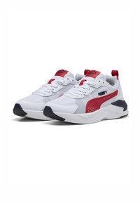 Para białych sportowych sneakersów z czerwonymi akcentami, czarnymi detalami na podeszwie oraz górą z materiału siatkowego, ustawiona pod kątem w prawo na białym tle.